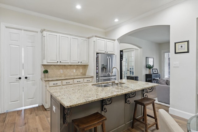 kitchen featuring light wood-type flooring, a sink, light stone counters, arched walkways, and stainless steel fridge with ice dispenser