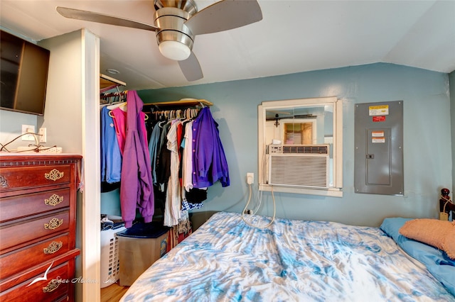 bedroom featuring cooling unit, a ceiling fan, wood finished floors, electric panel, and vaulted ceiling