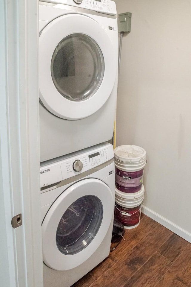 clothes washing area featuring laundry area, wood finished floors, baseboards, and stacked washer and dryer