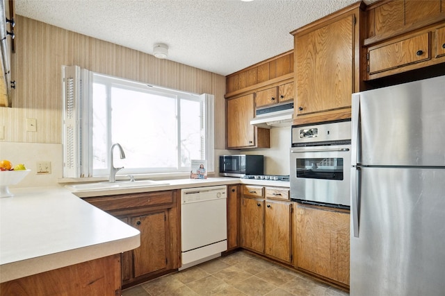 kitchen with brown cabinets, under cabinet range hood, a sink, appliances with stainless steel finishes, and light countertops