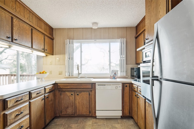 kitchen with brown cabinetry, white dishwasher, freestanding refrigerator, a sink, and light countertops