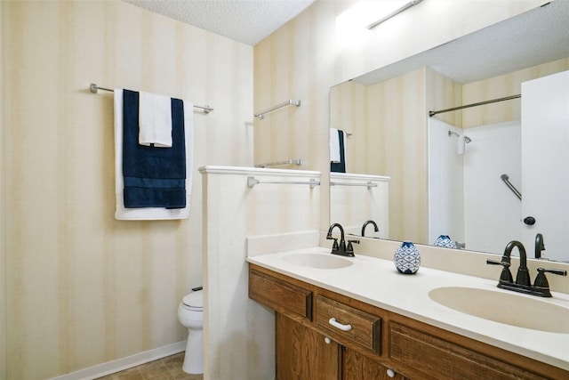 bathroom with double vanity, toilet, a textured ceiling, and a sink