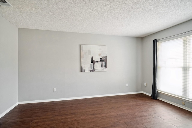 spare room featuring visible vents, a textured ceiling, baseboards, and dark wood-style flooring