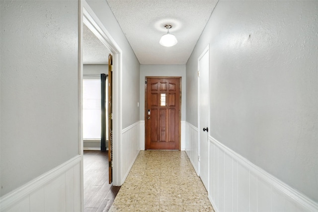 entryway featuring a textured ceiling, light floors, and wainscoting