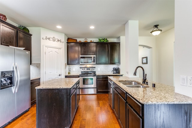 kitchen with a sink, appliances with stainless steel finishes, hardwood / wood-style flooring, and a kitchen island with sink