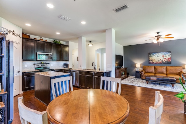 kitchen featuring visible vents, an island with sink, appliances with stainless steel finishes, arched walkways, and a sink