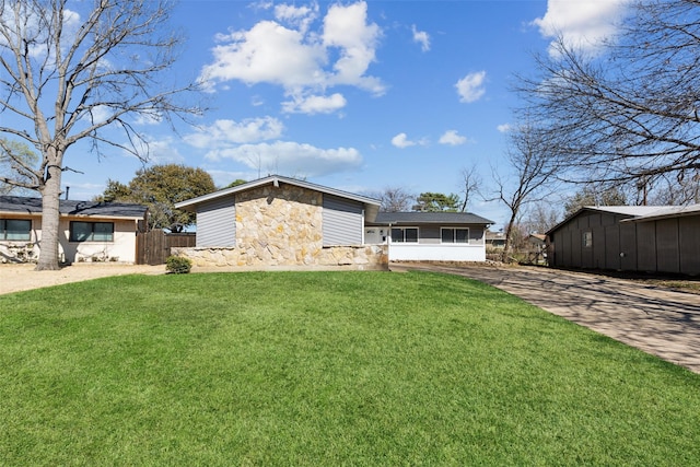 view of front of house with stone siding, concrete driveway, a front yard, and fence