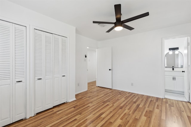 unfurnished bedroom with baseboards, ensuite bath, ceiling fan, multiple closets, and light wood-type flooring