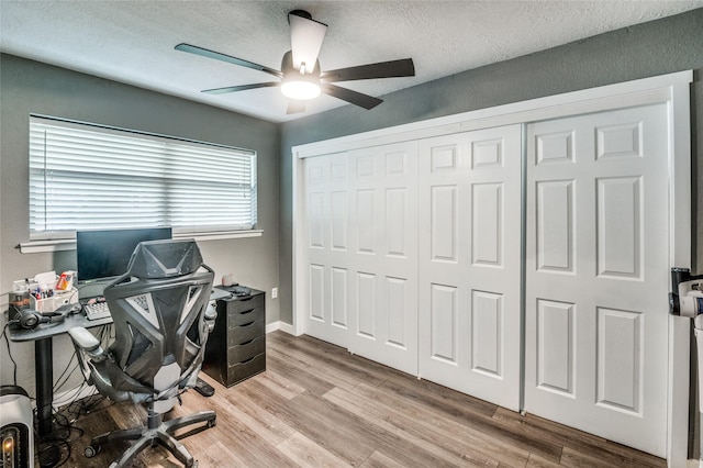 office space with baseboards, a textured ceiling, light wood-type flooring, and a ceiling fan