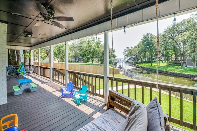 deck featuring a lawn, fence, a ceiling fan, and a water view