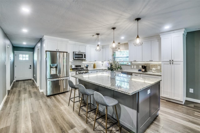 kitchen with stainless steel appliances, white cabinets, a center island, and light wood finished floors