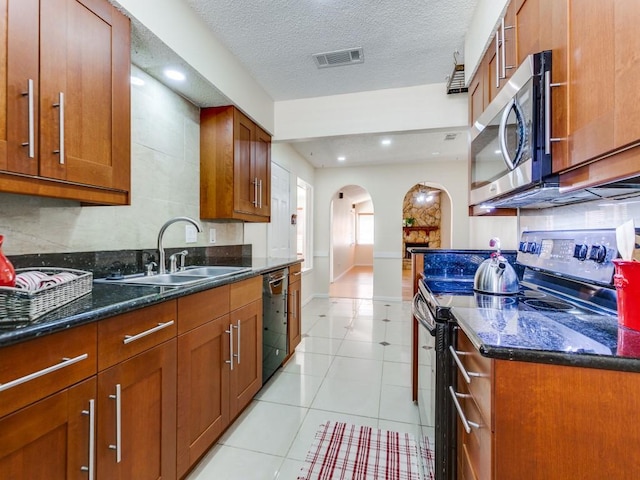 kitchen with visible vents, a sink, dark stone counters, arched walkways, and appliances with stainless steel finishes