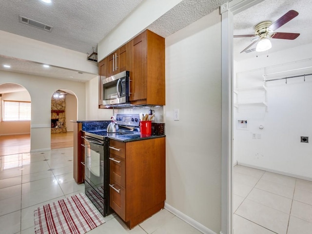 kitchen with brown cabinetry, visible vents, arched walkways, black range with electric cooktop, and stainless steel microwave