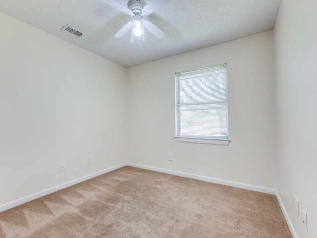 spare room with visible vents, baseboards, light colored carpet, a textured ceiling, and a ceiling fan