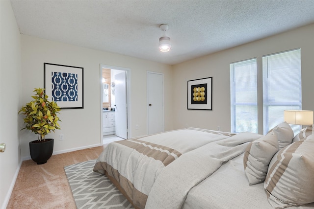 bedroom featuring ensuite bath, carpet flooring, baseboards, and a textured ceiling