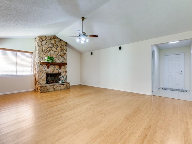 unfurnished living room featuring a ceiling fan, lofted ceiling, a stone fireplace, light wood-style floors, and a textured ceiling