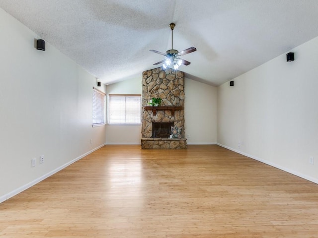 unfurnished living room featuring light wood finished floors, lofted ceiling, ceiling fan, a stone fireplace, and a textured ceiling