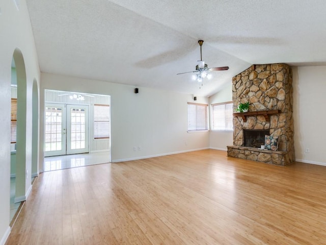 unfurnished living room with arched walkways, a textured ceiling, light wood-type flooring, and ceiling fan