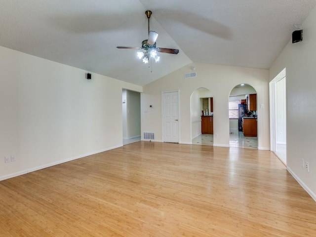 unfurnished living room with a ceiling fan, visible vents, lofted ceiling, arched walkways, and light wood-style floors