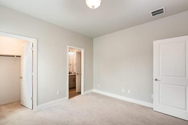 unfurnished bedroom with visible vents, a walk in closet, baseboards, light colored carpet, and ensuite bathroom