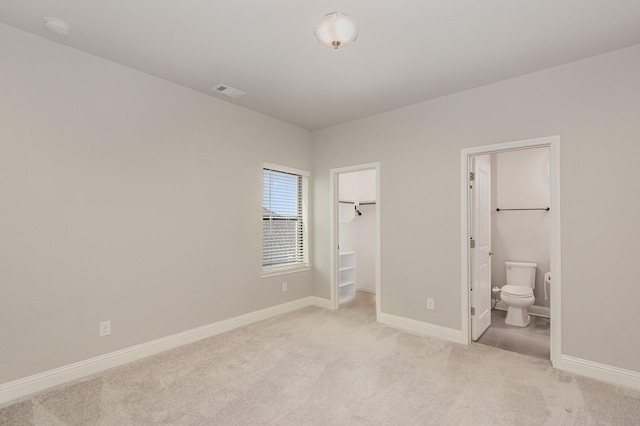 unfurnished bedroom featuring baseboards, visible vents, a spacious closet, ensuite bathroom, and light carpet