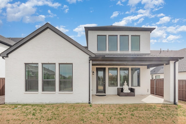 rear view of property featuring brick siding, a patio area, a lawn, and fence