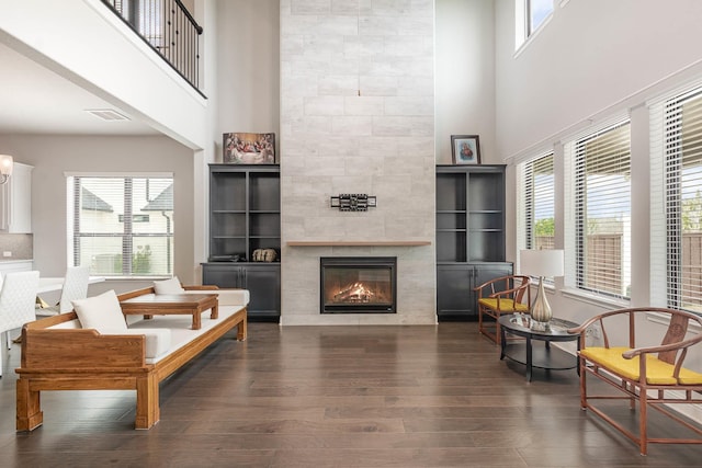 living room with a healthy amount of sunlight, a tile fireplace, dark wood-type flooring, and a high ceiling