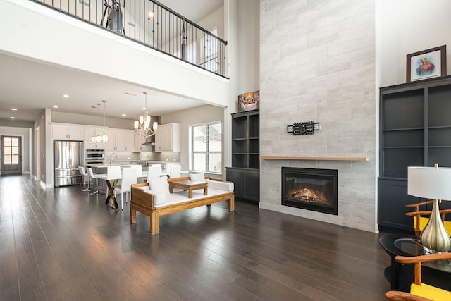 living area featuring dark wood-type flooring, a tiled fireplace, recessed lighting, a high ceiling, and a notable chandelier