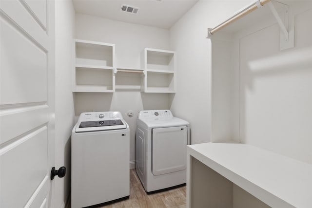 clothes washing area featuring light wood-type flooring, visible vents, laundry area, and washing machine and clothes dryer