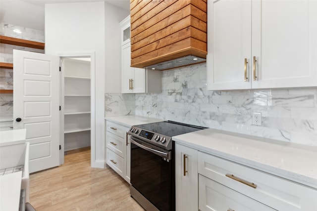 kitchen featuring light wood finished floors, stainless steel range with electric cooktop, custom range hood, white cabinetry, and backsplash