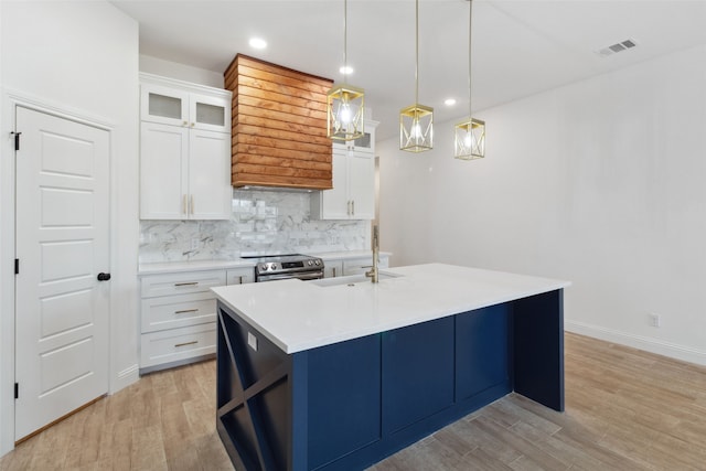 kitchen with electric range, visible vents, an island with sink, light wood finished floors, and decorative backsplash