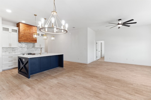 kitchen with a kitchen island with sink, tasteful backsplash, open floor plan, white cabinetry, and light countertops