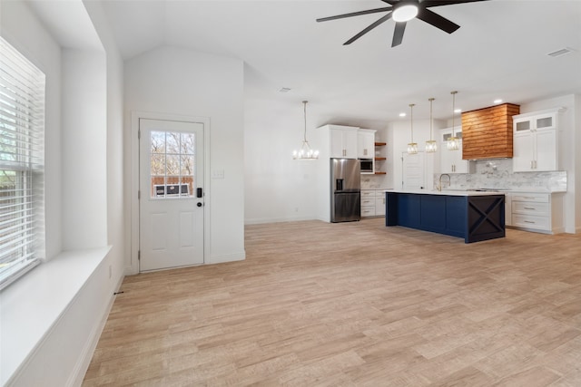 unfurnished living room with visible vents, baseboards, light wood-type flooring, vaulted ceiling, and ceiling fan with notable chandelier