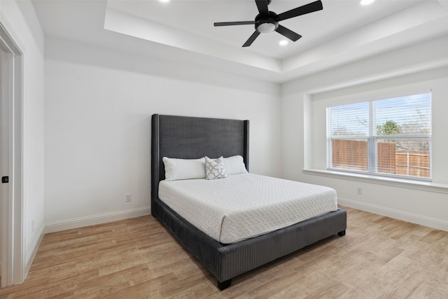 bedroom featuring light wood finished floors, recessed lighting, a raised ceiling, and baseboards