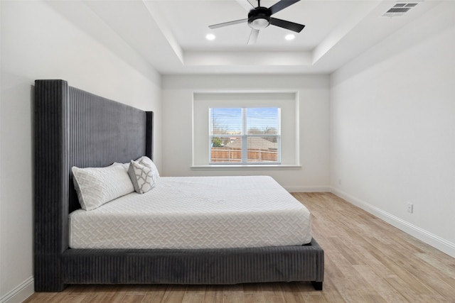 bedroom with visible vents, baseboards, a raised ceiling, and wood finished floors