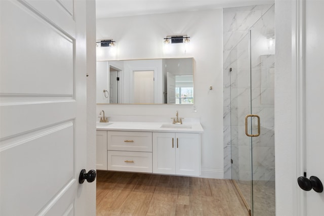 full bathroom with double vanity, wood finished floors, a marble finish shower, and a sink