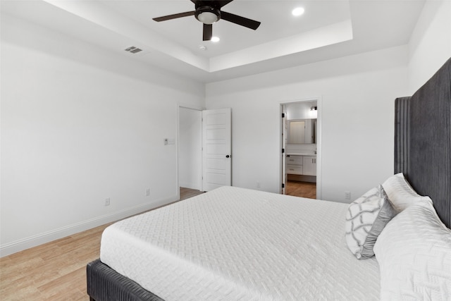 bedroom featuring a tray ceiling, wood finished floors, visible vents, and baseboards