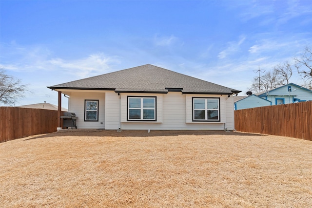 back of house with a fenced backyard and roof with shingles