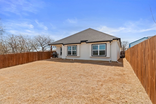 back of property with a fenced backyard and roof with shingles