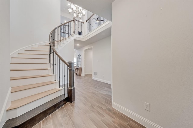 stairs featuring wood finished floors, visible vents, baseboards, a towering ceiling, and a chandelier