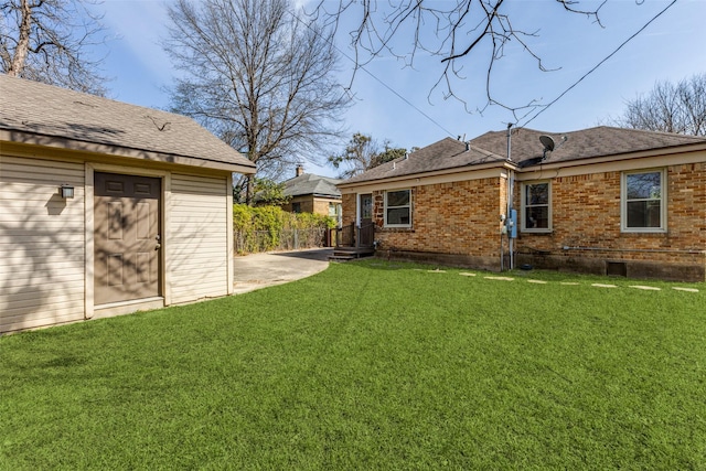 exterior space with brick siding, a shingled roof, a yard, and fence