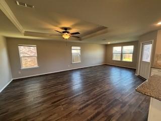 unfurnished living room with ornamental molding, a tray ceiling, dark wood finished floors, baseboards, and ceiling fan