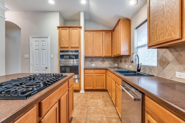 kitchen featuring a sink, tasteful backsplash, stainless steel appliances, arched walkways, and light tile patterned floors