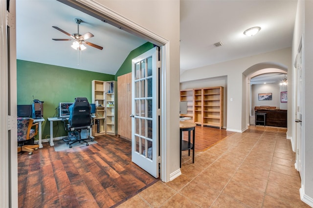 tiled office space featuring a ceiling fan, baseboards, visible vents, arched walkways, and vaulted ceiling