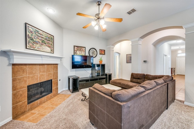 carpeted living room with a ceiling fan, visible vents, baseboards, arched walkways, and a tiled fireplace