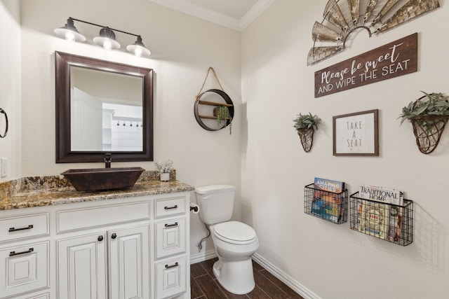 half bathroom with wood finish floors, toilet, crown molding, baseboards, and vanity