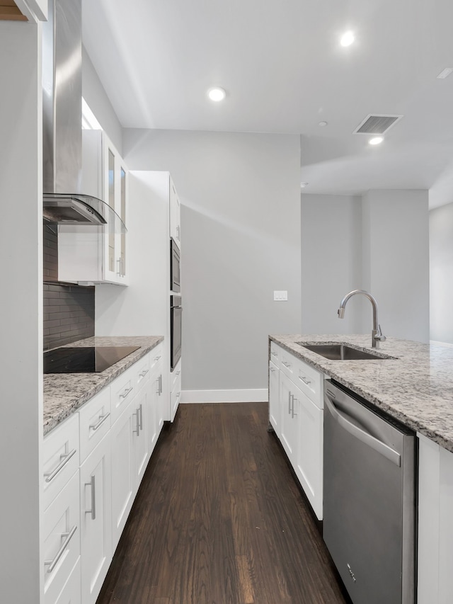 kitchen featuring visible vents, glass insert cabinets, appliances with stainless steel finishes, wall chimney exhaust hood, and a sink