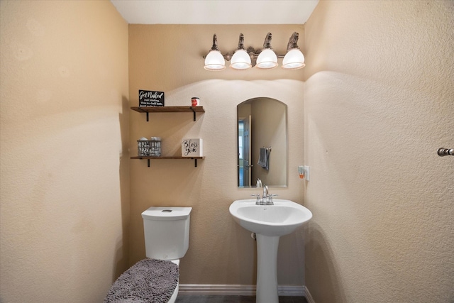 half bathroom featuring toilet, a textured wall, and a sink