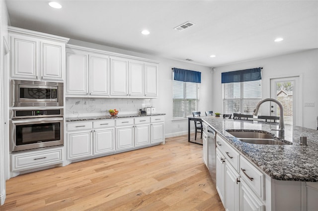 kitchen with light wood finished floors, decorative backsplash, white cabinets, stainless steel appliances, and a sink