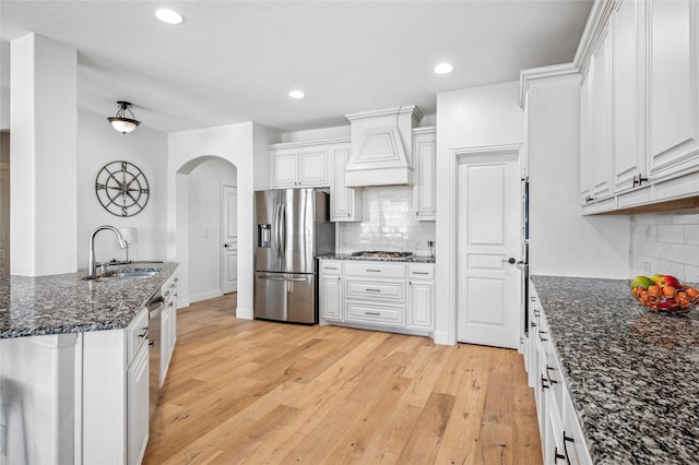 kitchen with light wood-style flooring, appliances with stainless steel finishes, arched walkways, custom exhaust hood, and a sink